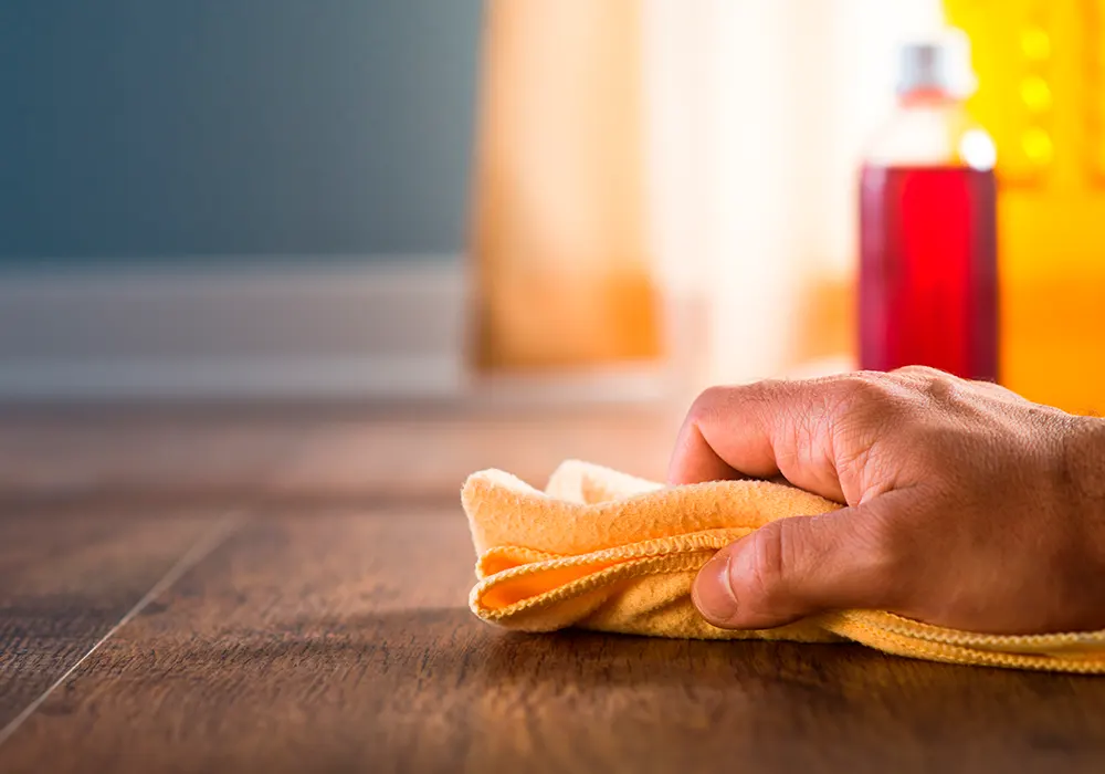 person waxing the hardwood with an orange cleaning cloth