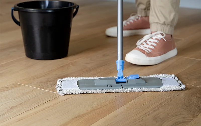 Man with a mop and a bucket, mopping a hardwood floor