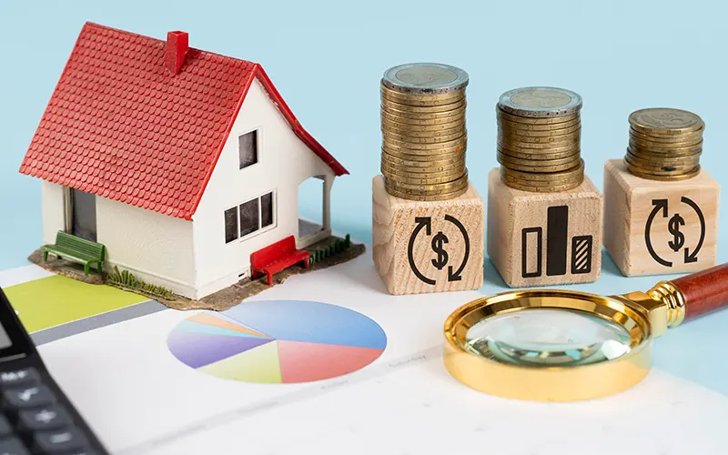 Table with a model of a house, some coins and a magnifying glass, under a pie chart