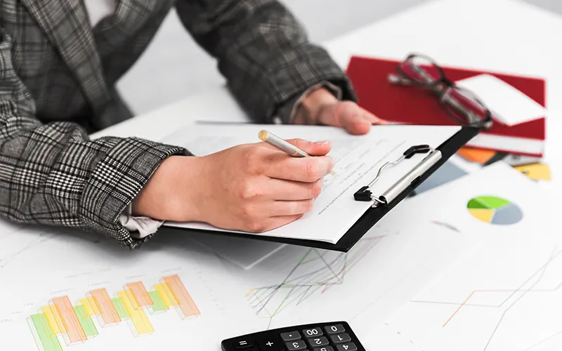 Table with investment documents and graphs, with an investor taking notes on a document