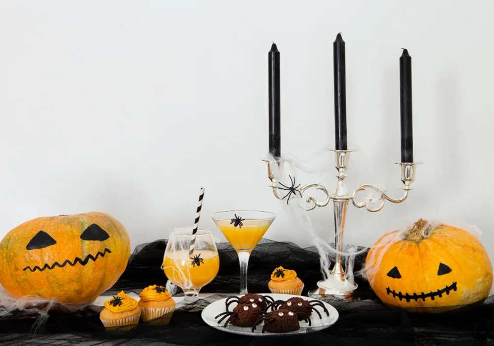 Halloween decorations, with painted pumpkins, spiders and webs decorating some cupcakes and juice glasses